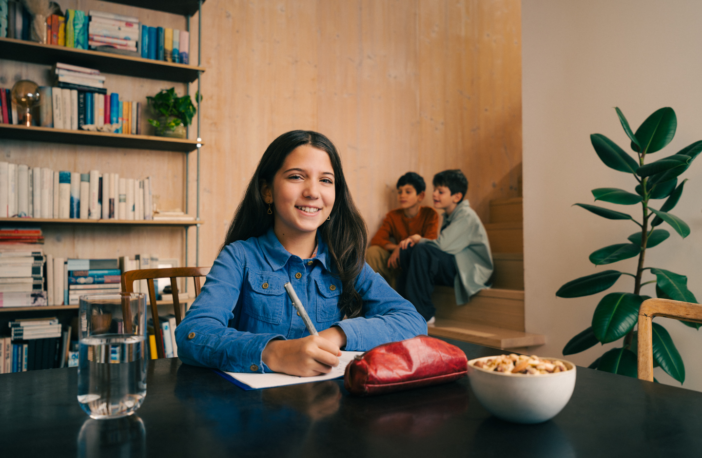 ein Mädchen mit langen braunen Haaren sitzt am Schreibtisch über ihrem Heft