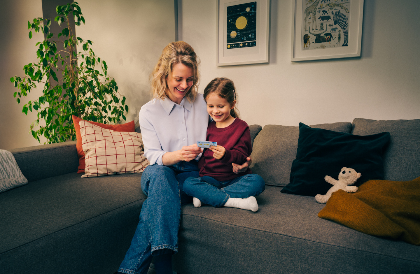 Mutter und Tochter sitzen auf der Couch und betrachten gemeinsam eine Volksbank Jugend Sparkarte.