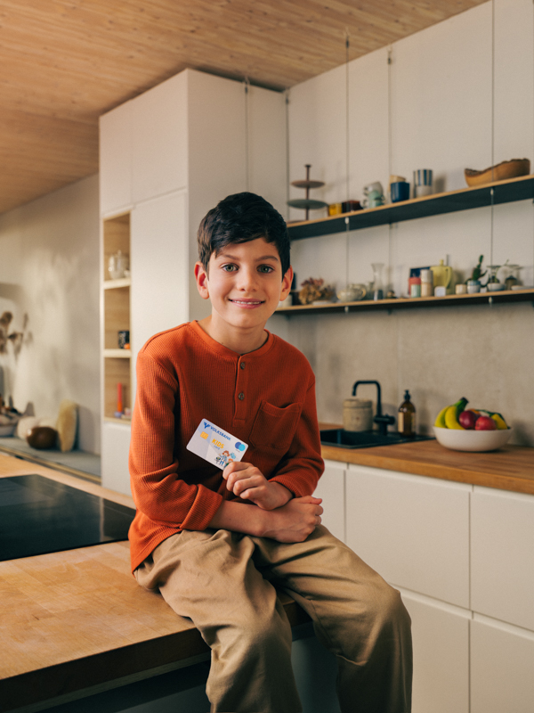 Ein Junge sitzt auf einem Tisch und hält die KidsCard in der Hand