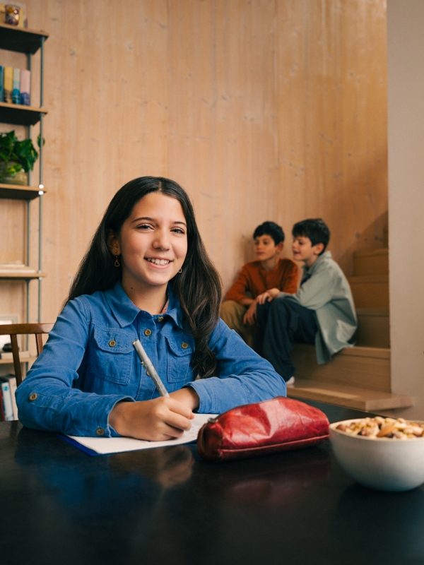 ein Mädchen mit langen braunen Haaren sitzt am Schreibtisch über einem Heft