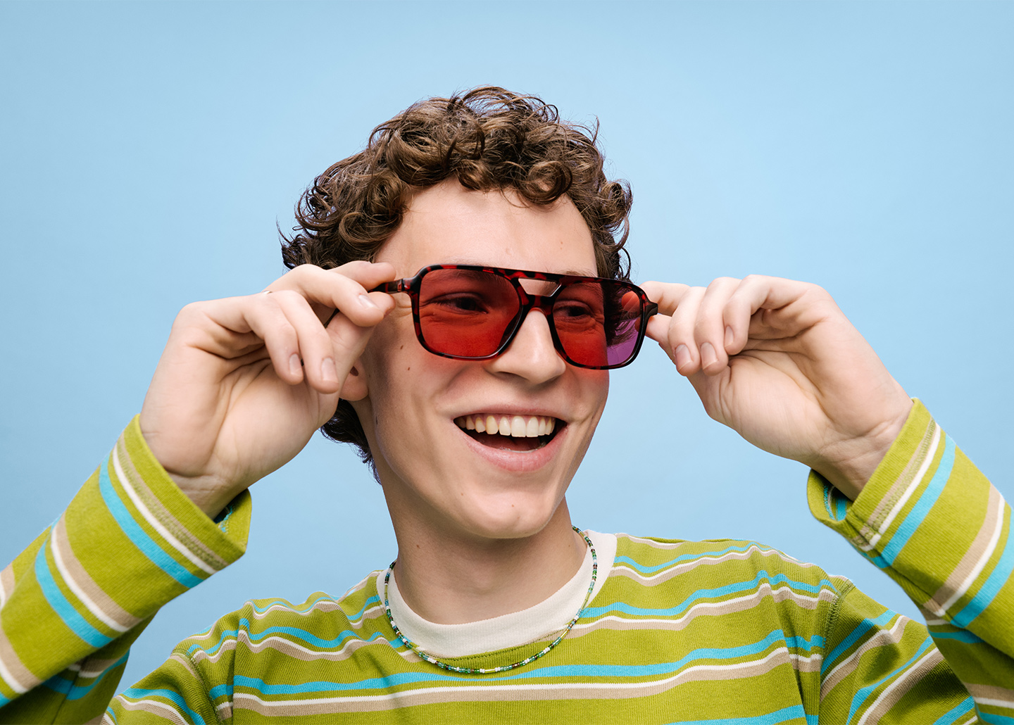 ein Jugendlicher mit grünem Pullover setzt sich eine Sonnenbrille auf