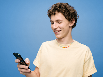 Jugendlicher mit Locken schaut lachend aufs Handy