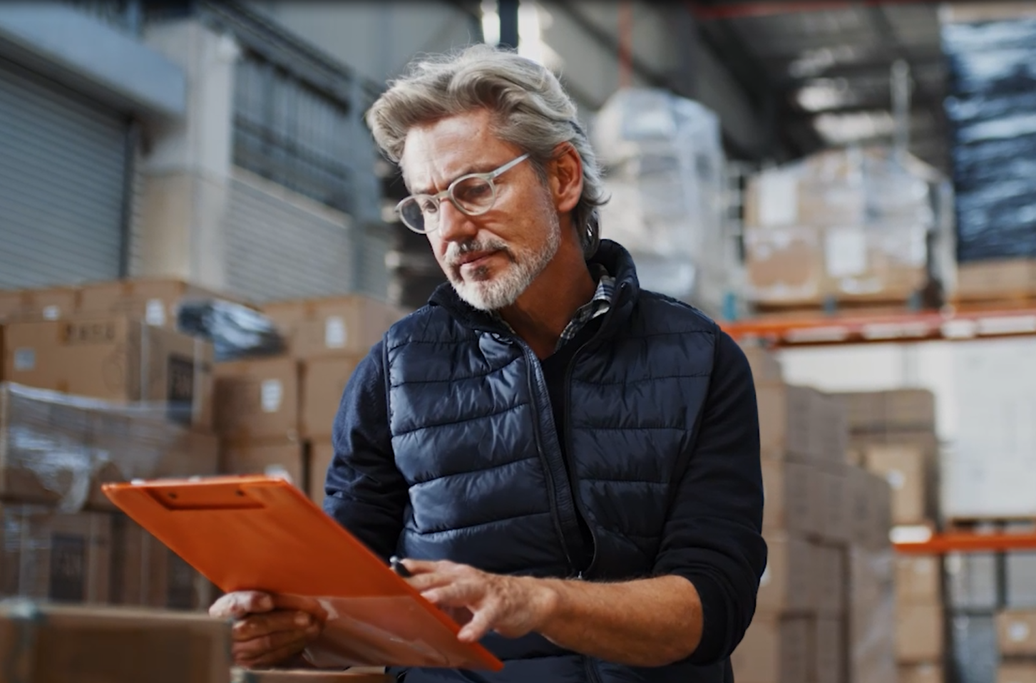 ein Mann mit grauen Haaren, Bart und Brille steht in einer Werkstatt und schaut auf sein Tablet