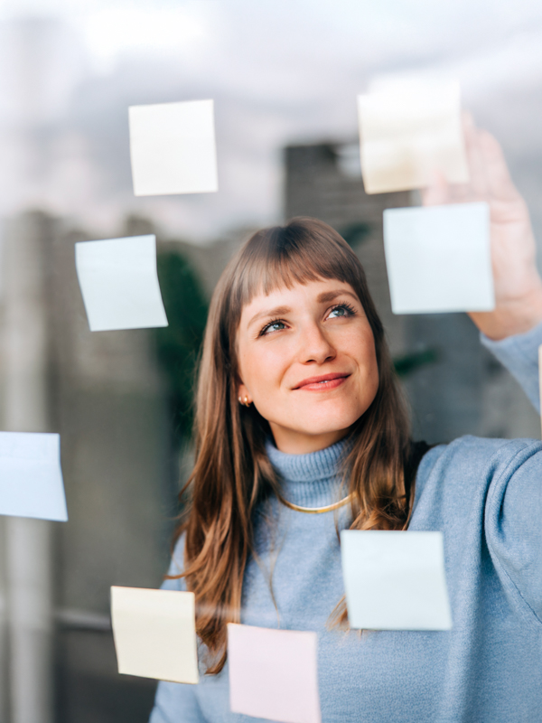 Eine Frau steht am Fenster an dem viele Post-It befestigt sind