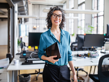 eine Frau mit Brille steht im Büro und lacht in die Kamera