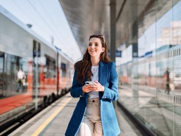 Eine Frau steht mit ihrem Handy am Bahnsteig