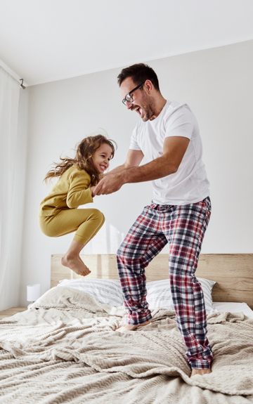 ein Vater springt mit seiner Tochter auf dem Bett