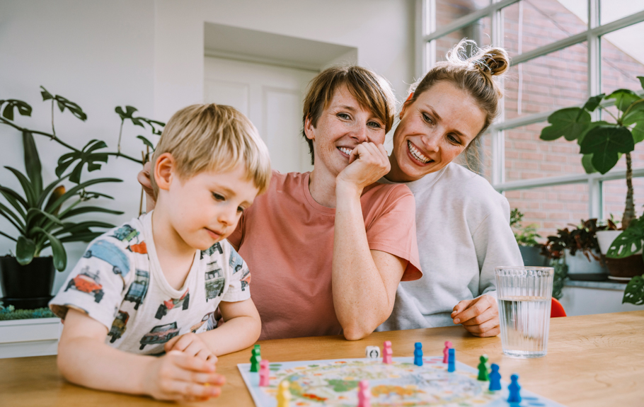 zwei Frauen und ein Kind sitzen am Tisch und spielen ein Brettspiel