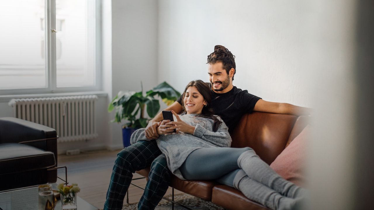 ein Pärchen liegt mit dem Handy auf der Couch