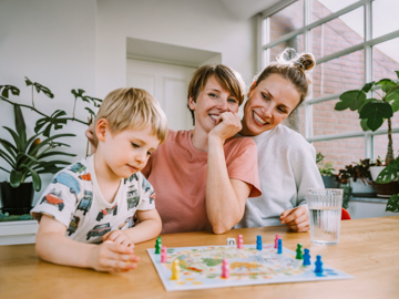 Zwei Frauen spielen mit einem Kind ein Brettspiel. 