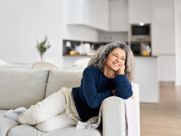 Eine Frau mit Locken liegt auf einer Sofa und lächelt. 