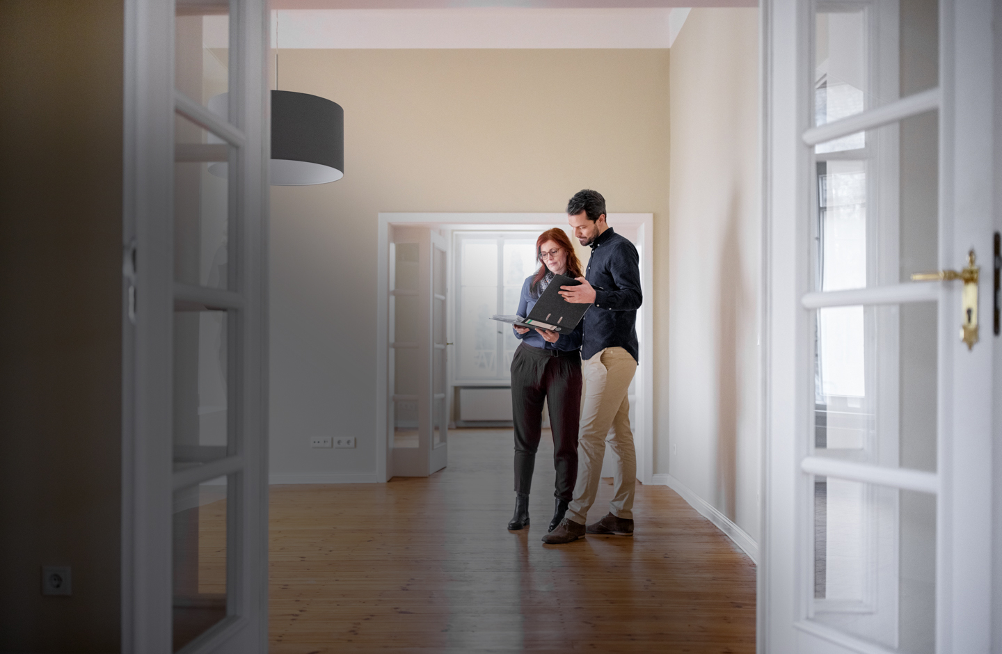 Ein junges Paar steht in einer Wohnung und sieht auf Unterlagen